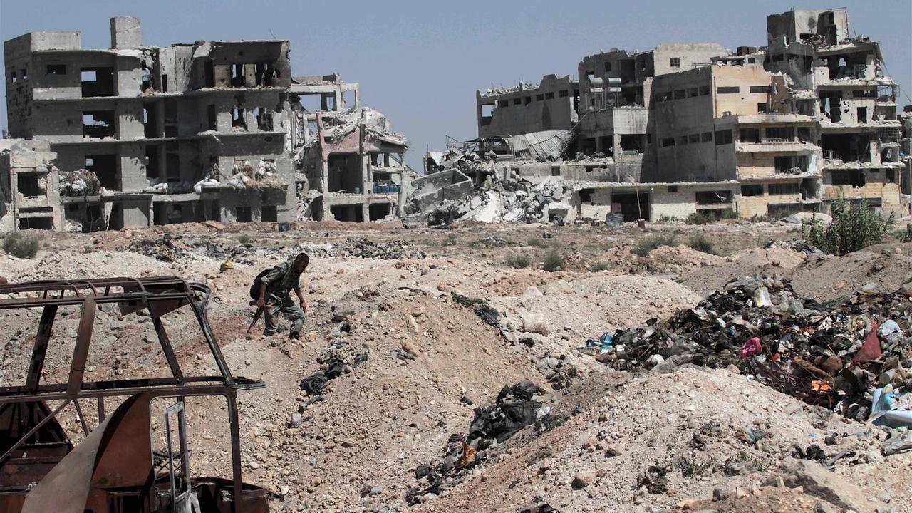 Ein Soldat läuft über Trümmerberge in Aleppo, im Hintergrund stehen die Ruinen mehrerer Häuser