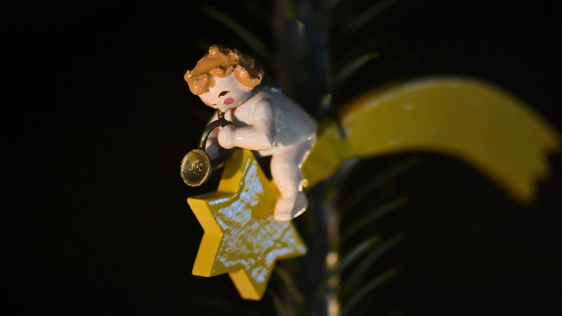Anhänger an einem Weihnachtsbaum: Ein Holzengel, der in ein Horn bläst, sitzt auf einem Stern mit Schweif.