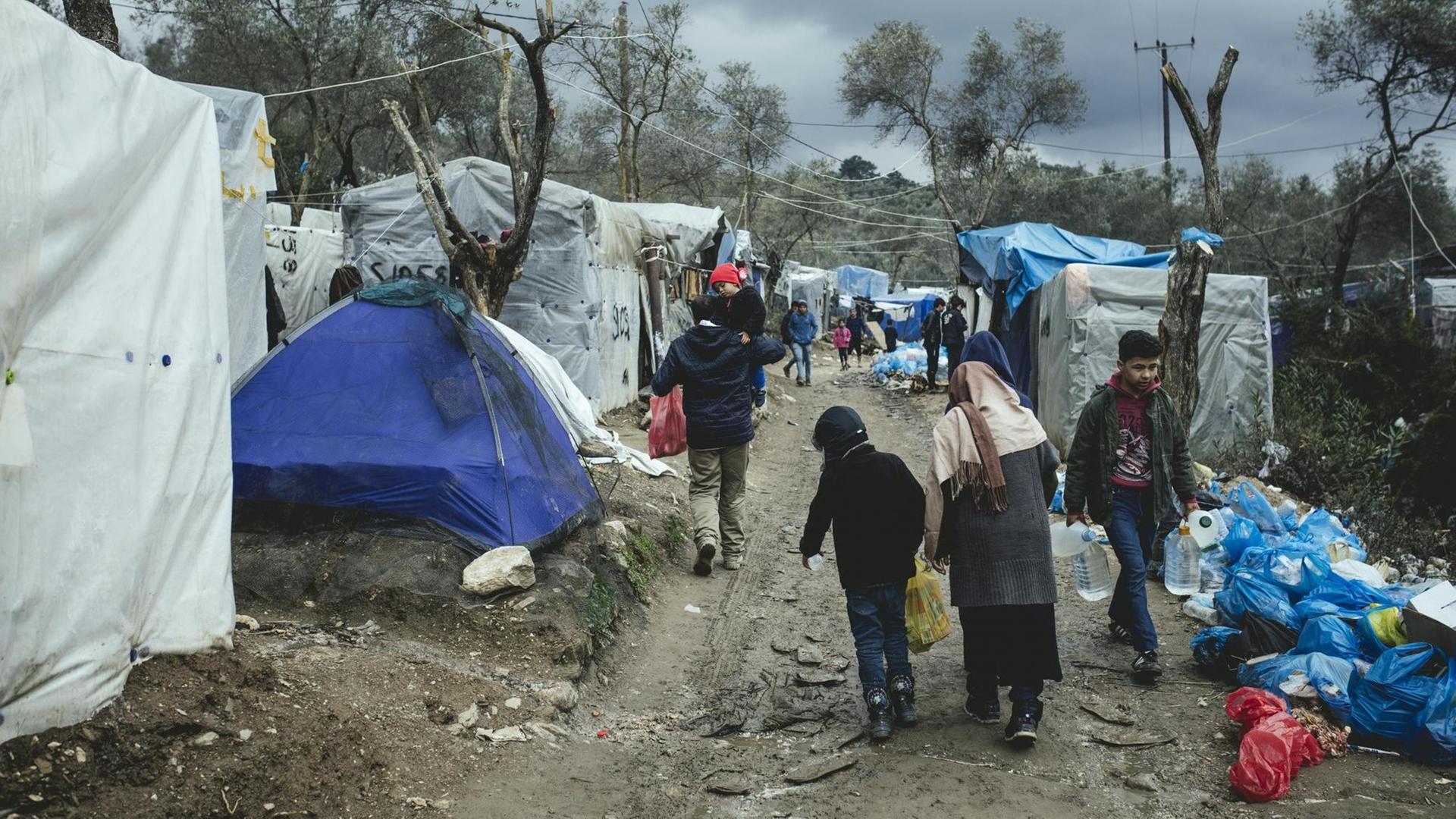 Eine Frau geht mit Kindern durch ein Flüchtlingslager, in welchem desolate Verhältnisse herrschen.