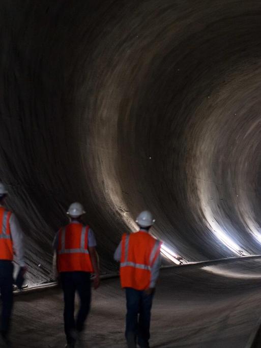 Drei Männer in Warnwesten gehen durch einen Tunnel des Bahnprojektes Stuttgart 21.