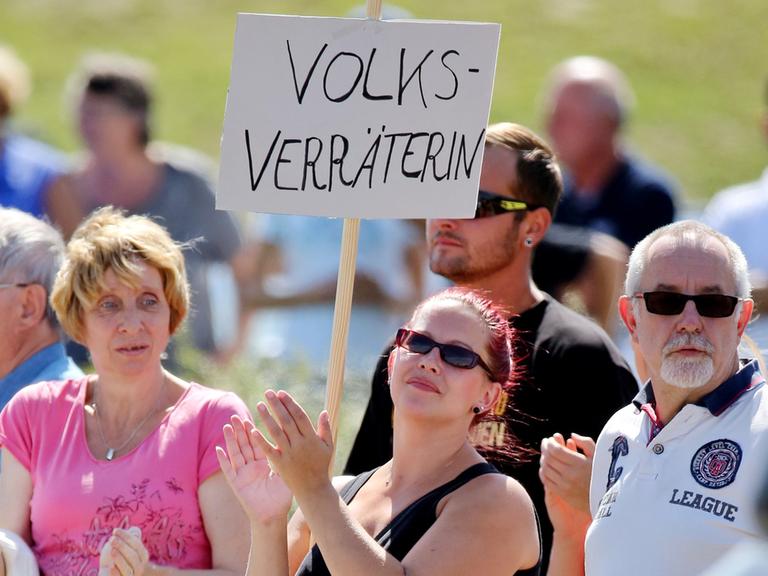 Eine Frau steht mit einem Schild "Volksverräterin" am 26.08.2015 vor einer Flüchtlingsunterkunft in Heidenau (Sachsen) und wartet auf Bundeskanzlerin Merkel. Die Kanzlerin besucht die Flüchtlingsunterkunft.