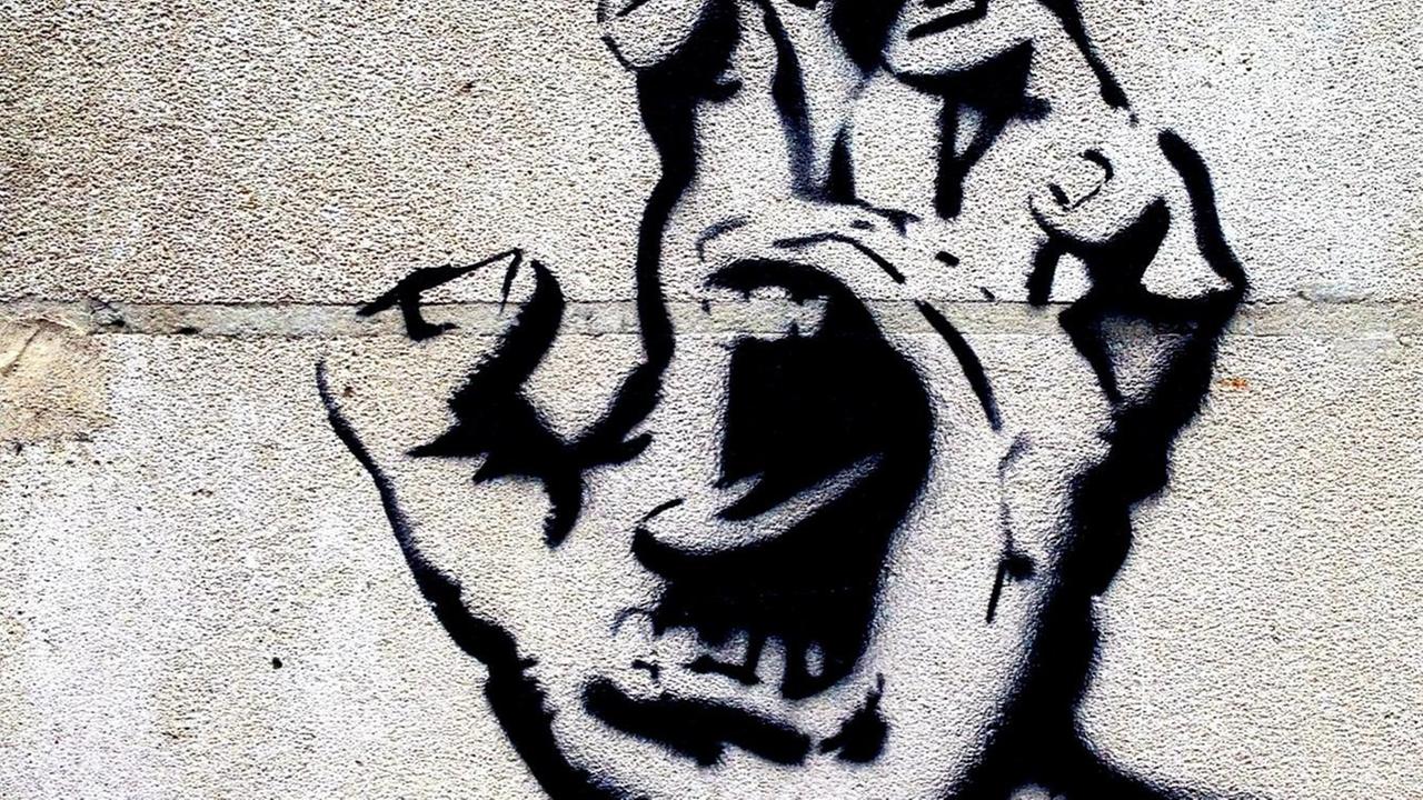 Ein Grafitti zeigt eine Handfläche in deren Mitte ein Mund aufgerissen schreit.