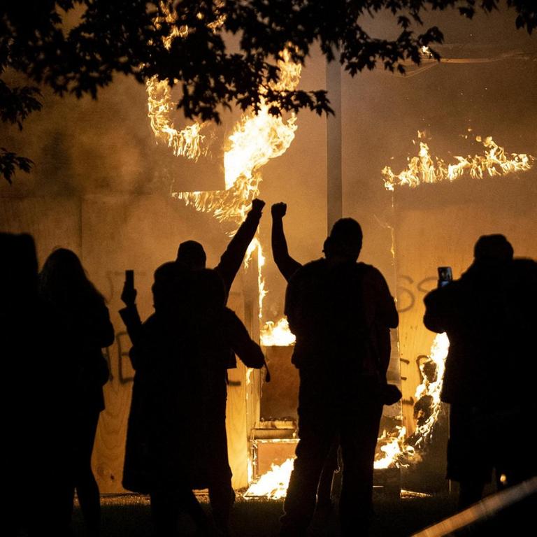 Menschen als Silhouetten vor einem brennenden Geschäft, das im Zuge der Unruhen in Brand gesteckt wurde.