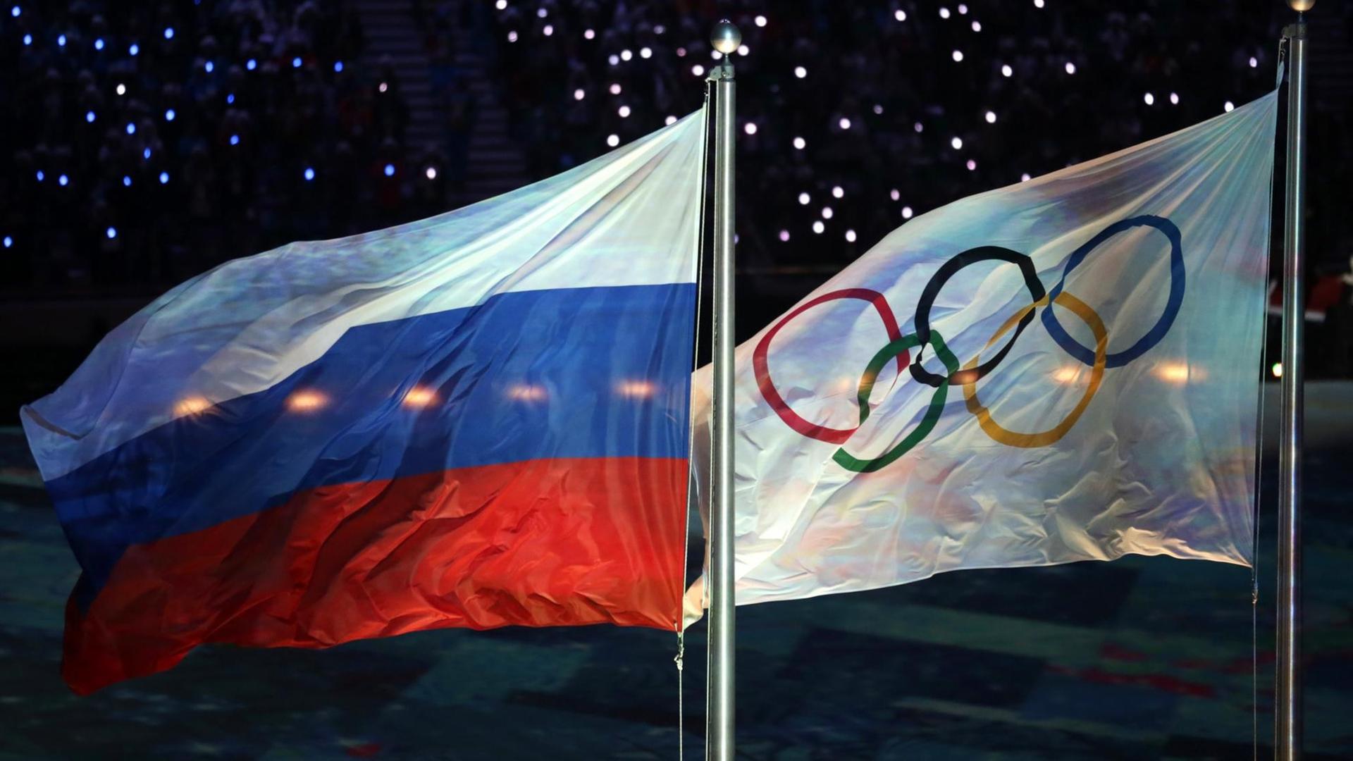 Die Olympische Flagge (r) und die russische Flagge flattern am 23.02.2014 während der Abschlussfeier bei den Olympischen Spielen 2014 in Sotschi, Russland.