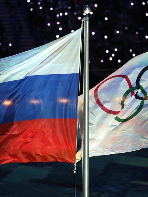 Die Olympische Flagge (r) und die russische Flagge flattern am 23.02.2014 während der Abschlussfeier bei den Olympischen Spielen 2014 in Sotschi, Russland.