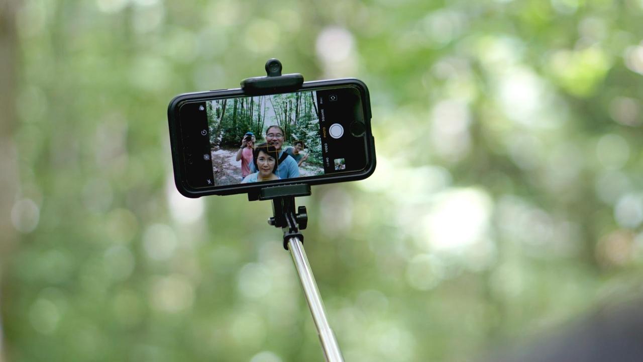 Ein Smartphone an einem Selfie-Stick for grünem Hintergrund in der Natur.