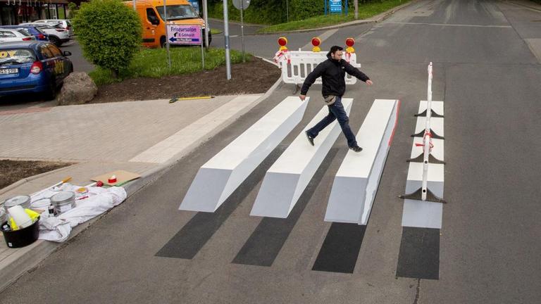 Der Graffitikünstler Alexander Frank aus Floh-Seligenthal springt über den halb fertigen 3D-Zebrastreifen im Wohngebiet Walperloh in Schmalkalden.