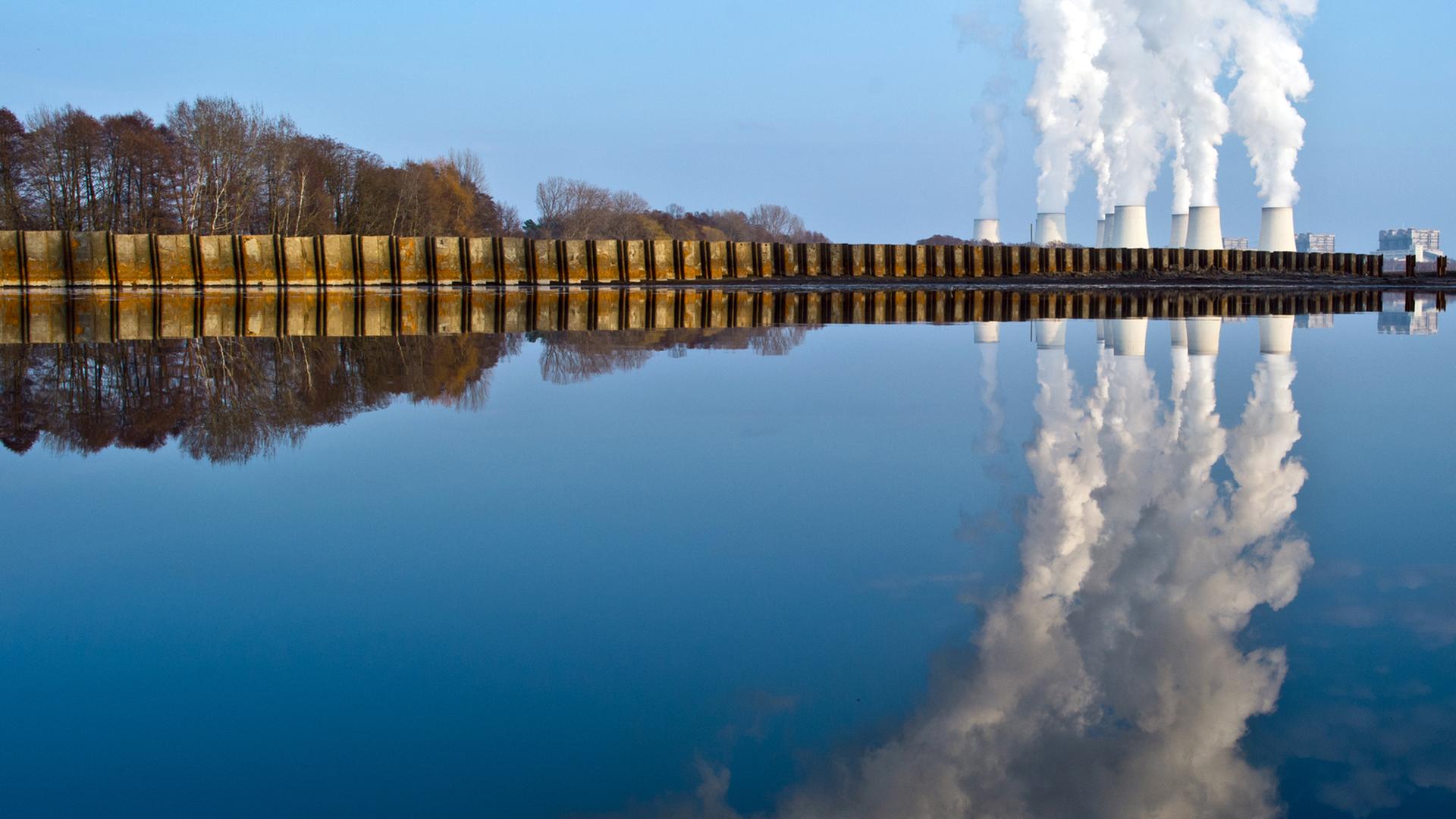 Wasserdampf steigt aus den Kühltürmen eines Braunkohlekraftwerks in Jänschwalde und spiegelt sich dabei in einem abgelassenen Fischteich. 