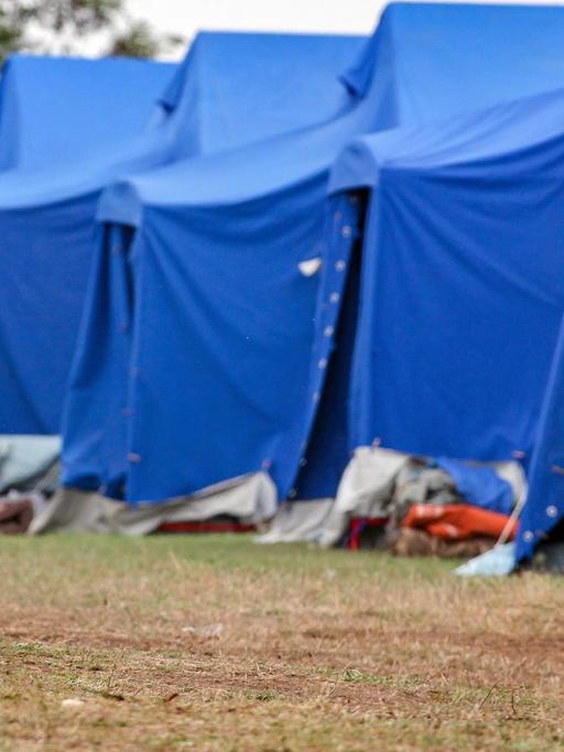Ein mann steht vor einer Reihe blauer Zelte und wischt sich den Schweiß von der Stirn.