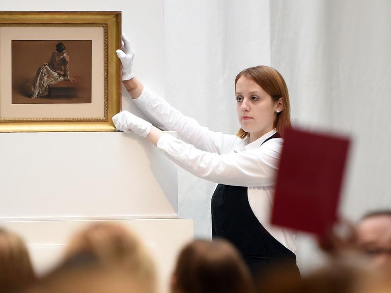 Eine Mitarbeiterin der Villa Grisebach präsentiert in Berlin bei einer Auktion das Werk "Emilie in roter Bluse" von Adolph Menzel. 