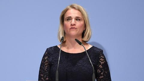 Eine blonde Frau steht an einem Rednerpult und spricht.