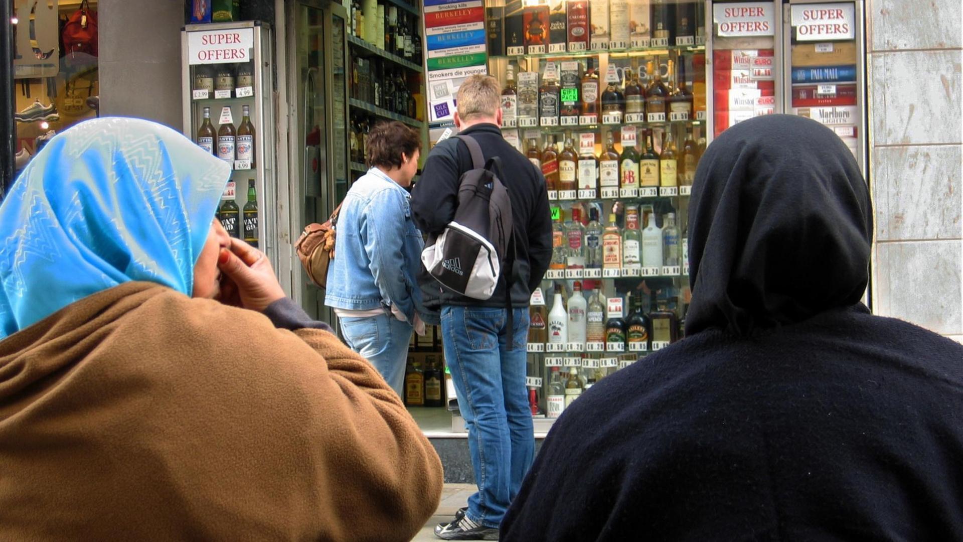 Zwei Musliminnen vor einem Laden mit Tabakwaren und alkoholischen Getränken