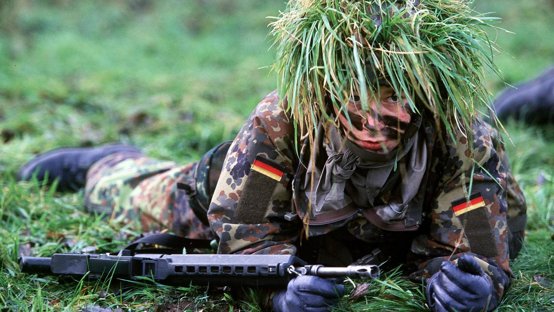 Eine Bundeswehrsoldatin robbt getarnt über eine Wiese.