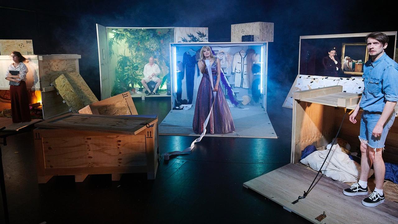 Bühne auf der große Holzcontainer stehen aus denen Schauspieler schauen.