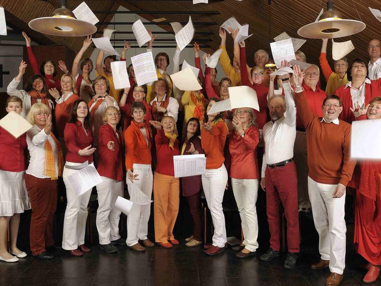 Gruppenfoto des Chors Lampenfieber aus Bergisch-Gladbach. Die Sängerinnen und Sänger werfen Notenblätter in die Luft.