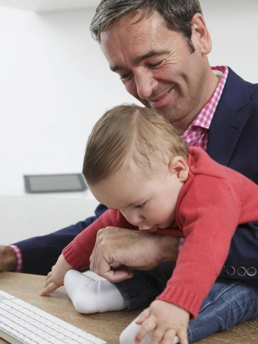 Symbolfoto: Geschäftsmann mit Baby im Arm im Homeoffice