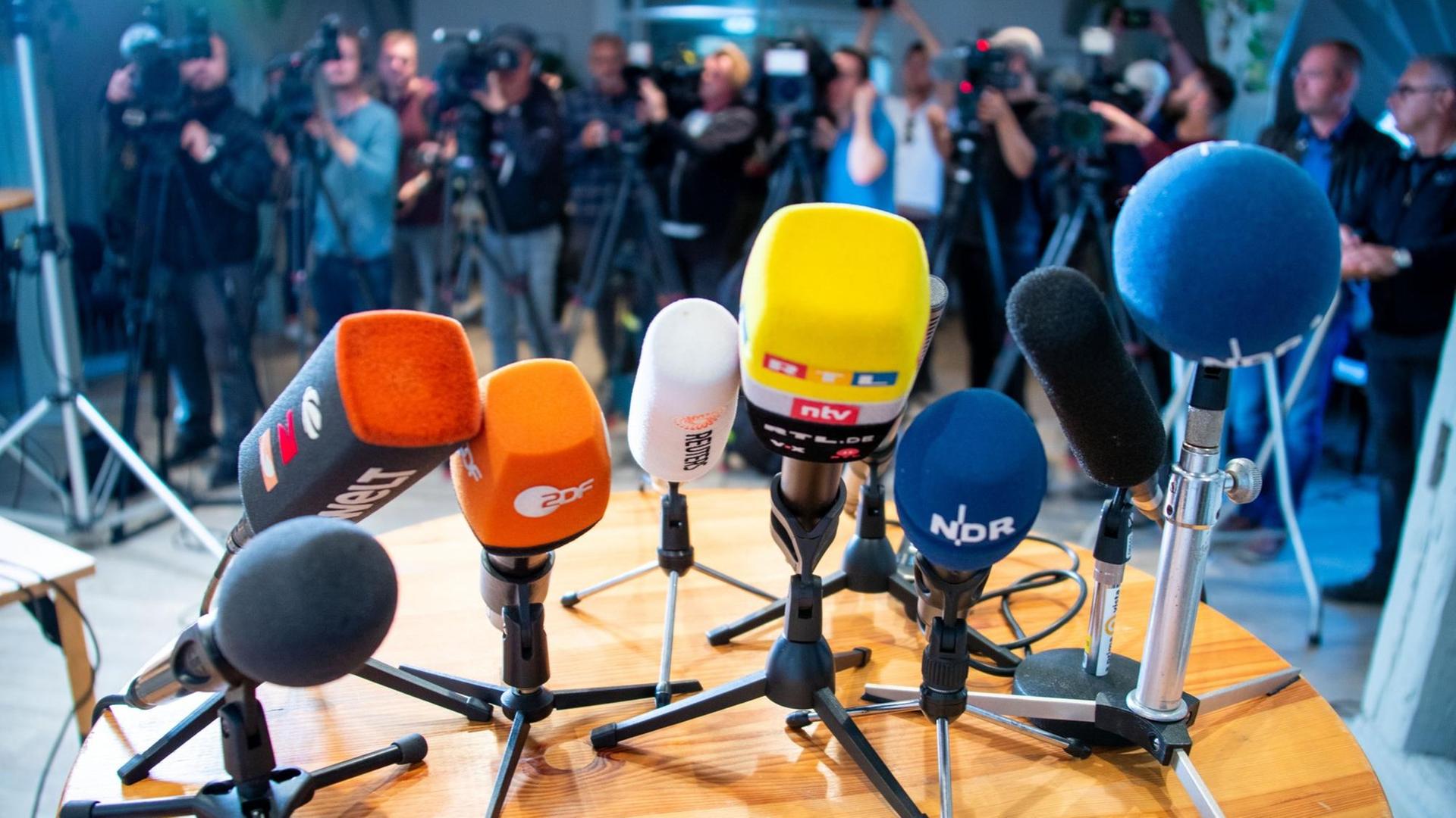 Bei einer Pressekonferenz sind Mikrofone auf einem Tisch platziert und Kameras aufgebaut.