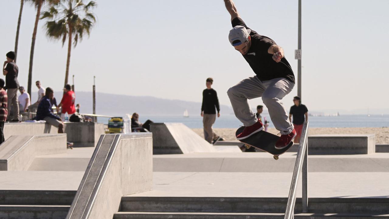 Ein Skater fährt ein Treppengeländer am Strand von Venice, Los Angeles herunter.