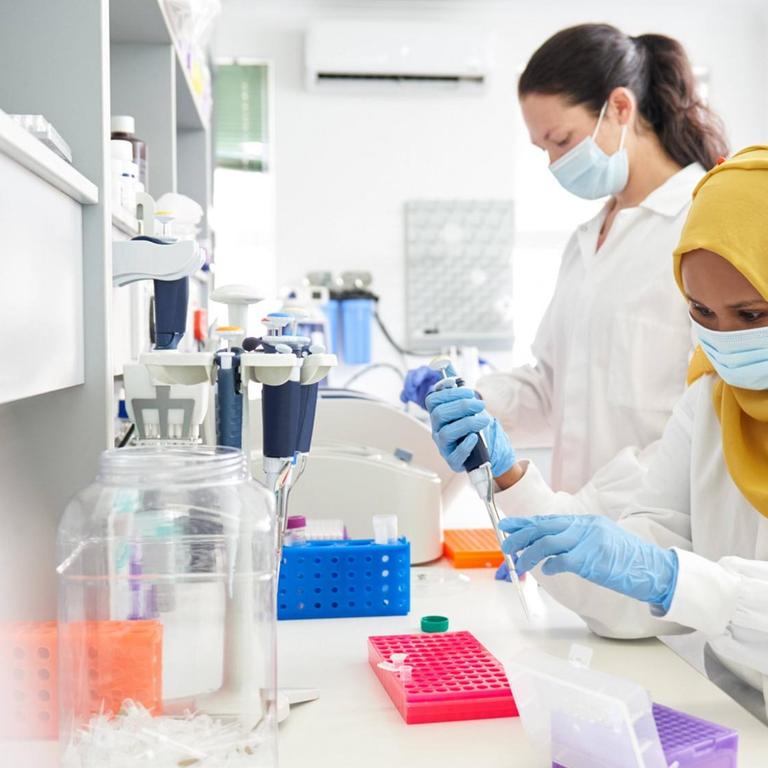 Zwei Wissenschaftlerinnen mit Maske, eine mit Hijab, arbeiten in einem Labor