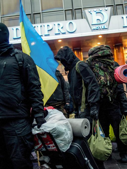 Eine Reihe von Männern, zum Teil vermummt oder mit Kaputzen, steht mit Koffern in der ukrainischen Hauptstadt Kiew.
