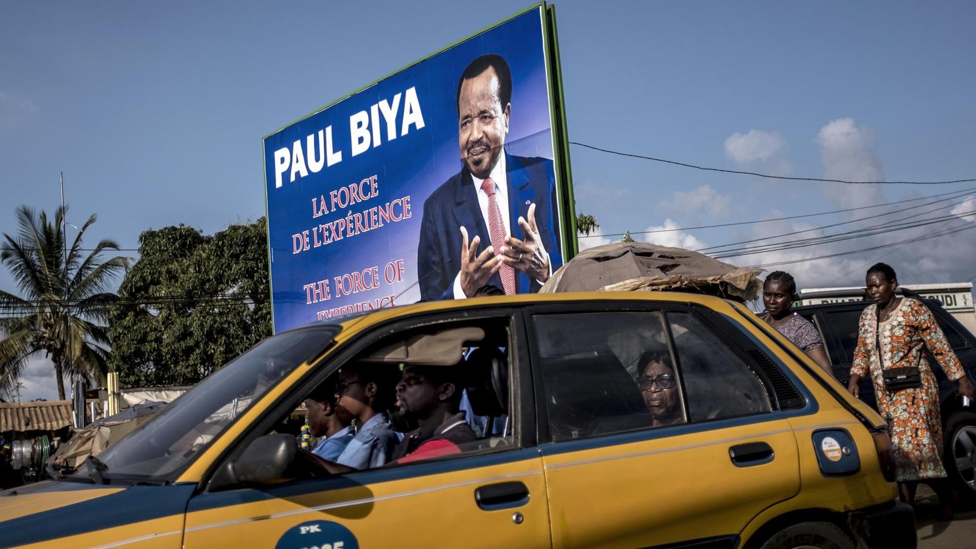 Ein Taxi fährt kurz vor der Präsidentschaftswahl in Kamerun in Yaoundé an einem Wahlplakat für Präsident Paul Biya vorbei / AFP PHOTO / MARCO LONGARI
