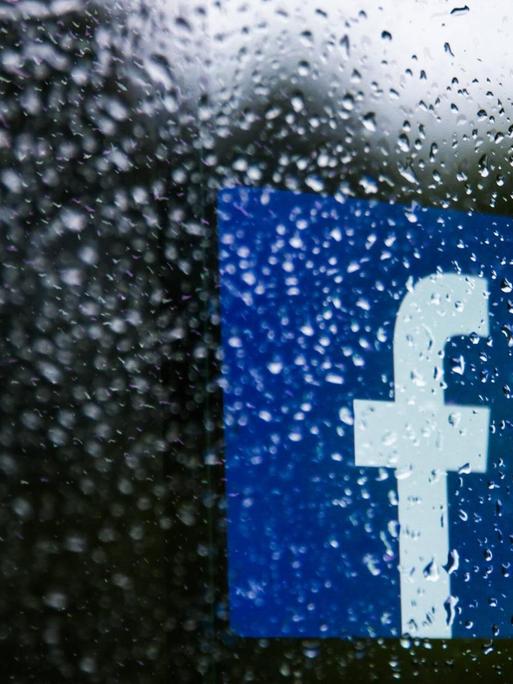Das Logo von Facebook hinter einer Scheibe mit Regentropfen