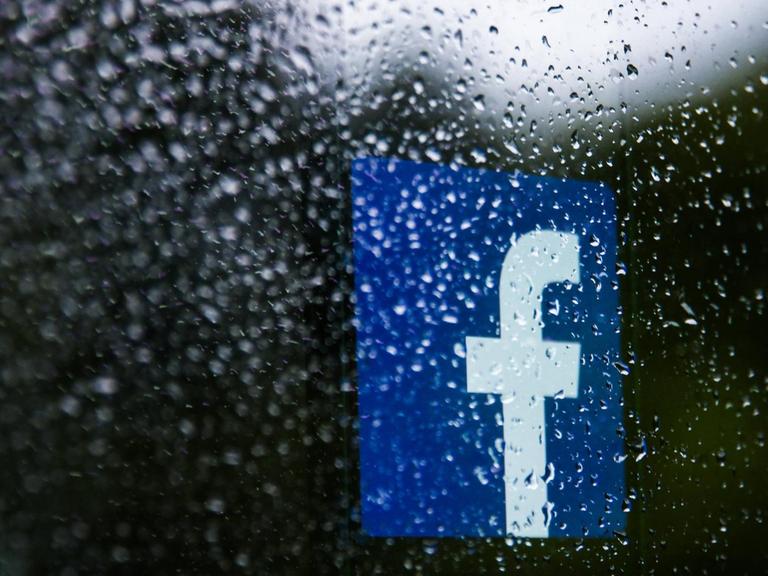Das Logo von Facebook hinter einer Scheibe mit Regentropfen