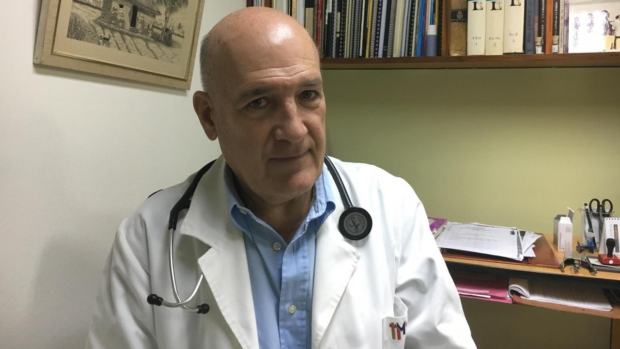 Der Direktor des Tropeninstituts von Caracas, Oscar Noya, sitzt in einem weißen Kittel und mit einem Stetoskop um den Hals in seinem Arbeitszimmer.