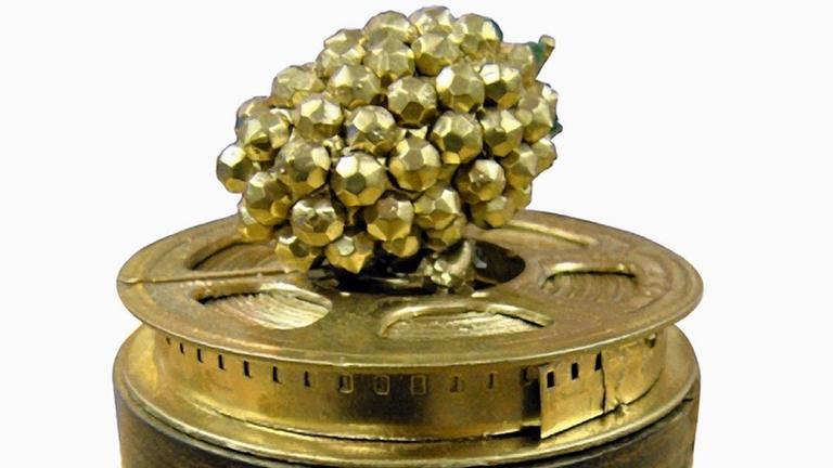 Das Bild zeigt den Anti-Filmpreis "Golde Himbeere". Er besteht aus der namensgebenden Frucht in goldener Farbe, die sich auf einer golden Filmrolle befindet.