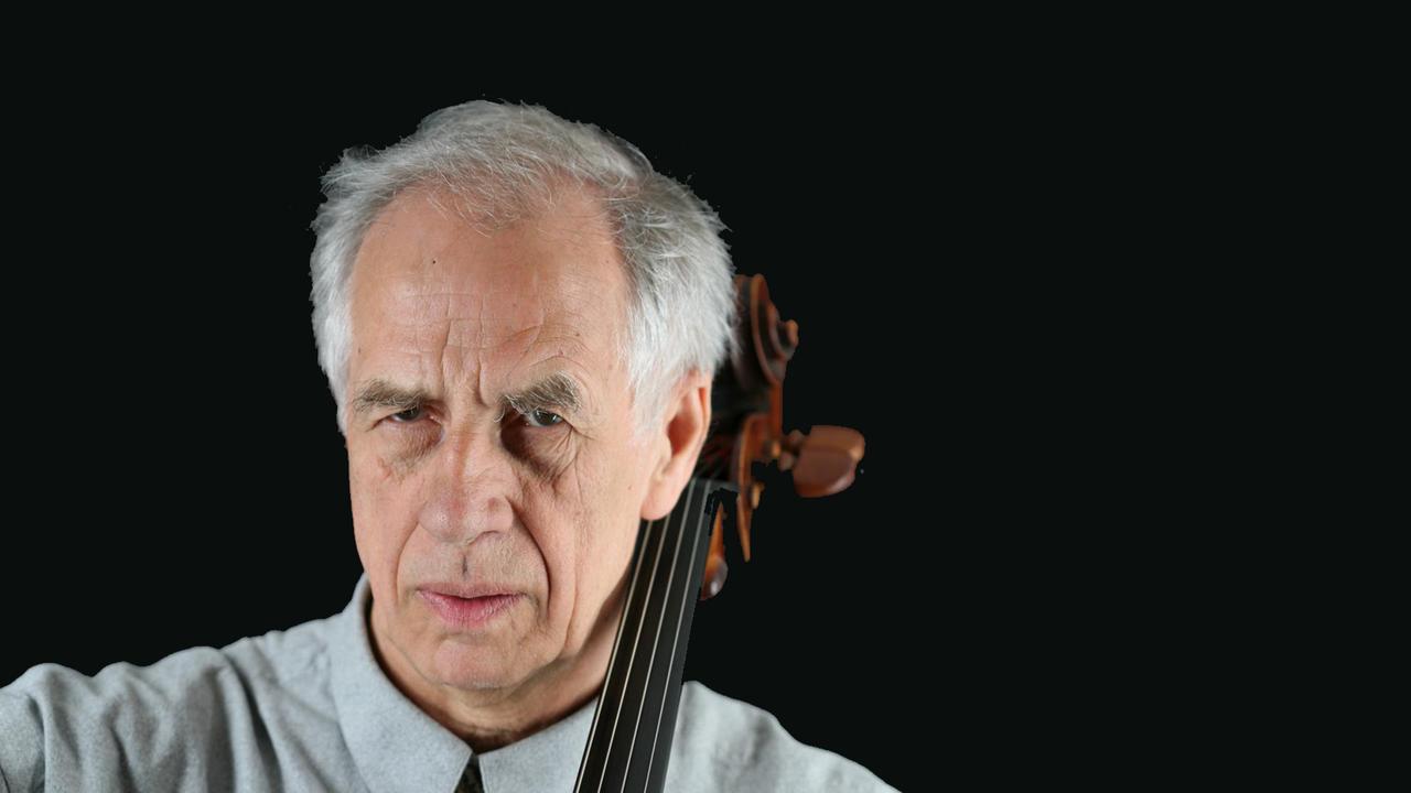 Ein Mann blickt ernst in die Kamera. Neben seinem Kopf sieht man die Schnecke seines Violoncellos. Es ist der Cellist Wolfgang Boettcher.