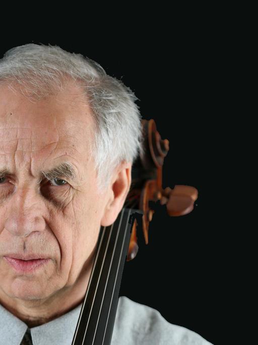 Ein Mann blickt ernst in die Kamera. Neben seinem Kopf sieht man die Schnecke seines Violoncellos. Es ist der Cellist Wolfgang Boettcher.