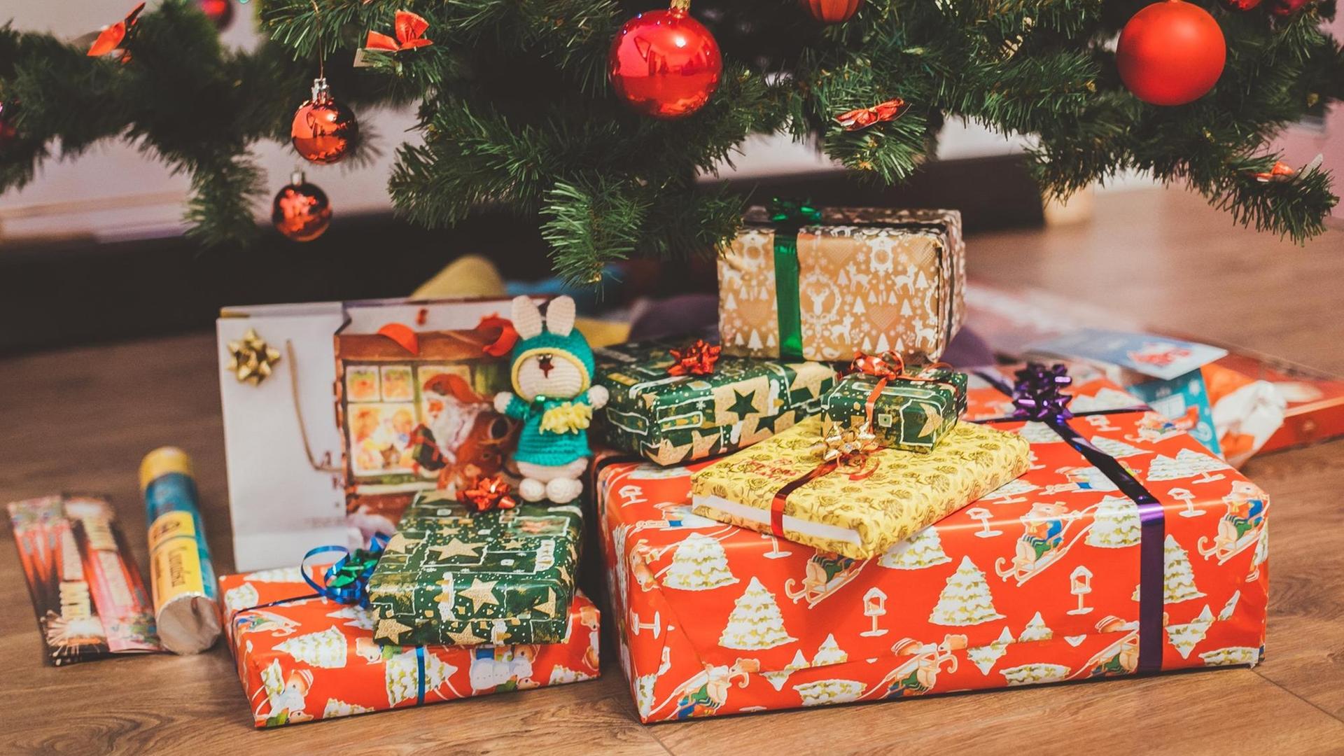 Ein Stapel bunt verpackter Geschenke unter einem geschmückten Weihnachtsbaum.