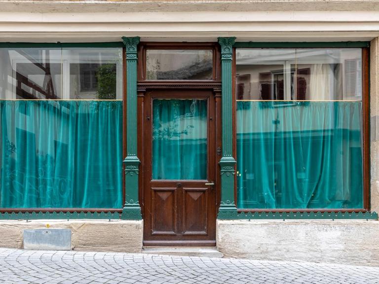 Leeres Ladengeschäft mit geschlossenen, türkisfarbenen Vorhängen im Schaufenster, in der Innenstadt von Tübingen.