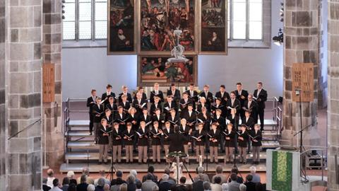 Ein Knabenchor steht im Altarraum einer großen Kirche und singt.