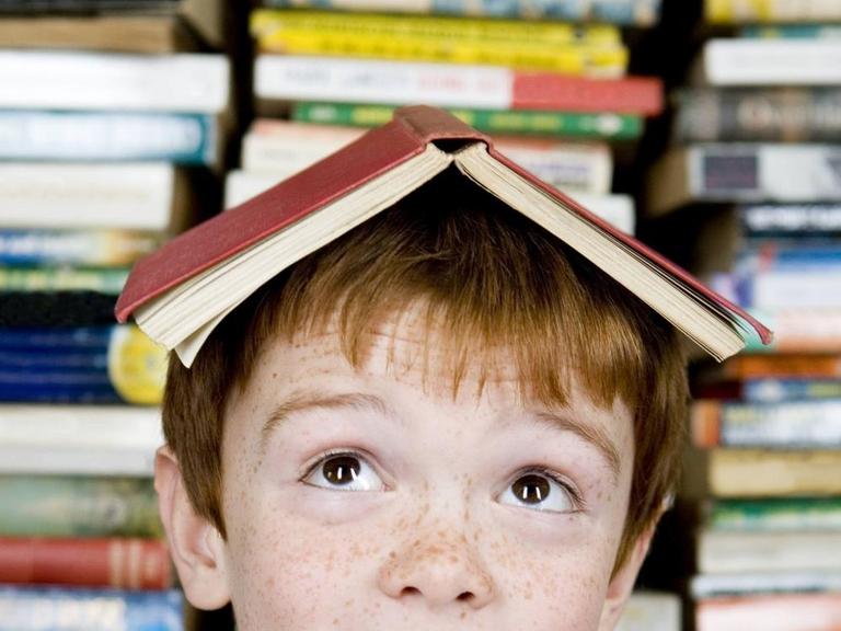 Ein rothaariger Junge mit einem Buch auf dem Kopf.