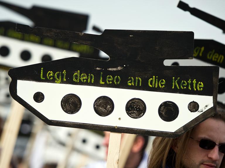 Ein Demonstrant trägt ein Schild in Form eines Panzers aus Holz mit der Aufschrift "Legt den Leo an die Kette"