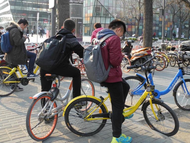 Schulkinder fahren in Peking mit Fahrrädern unterschiedlichster Anbieter.