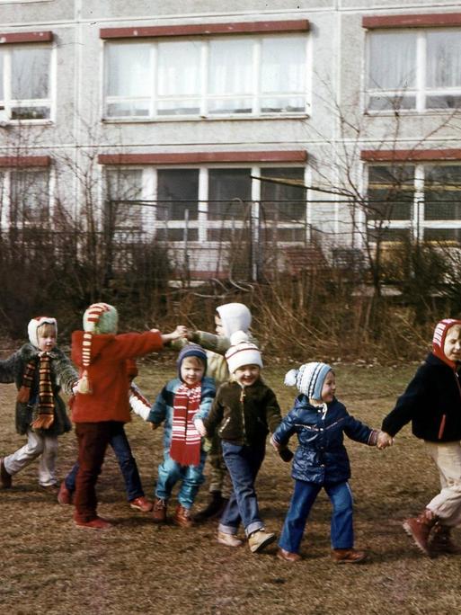 Historische Farbfotografie von Kindergartenkindern und einer Erzieherin, die sich alle an den Händen halten