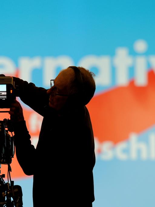 Ein Kameramann baut vor einer Wand mit dem Logo der Partei Alternative für Deutschland (AfD) eine Kamera auf.