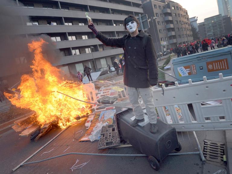 Ein Blockupy-Aktivist demonstriert vor einer brennenden Barrikade am 18.03.2015 in Frankfurt (Hessen).