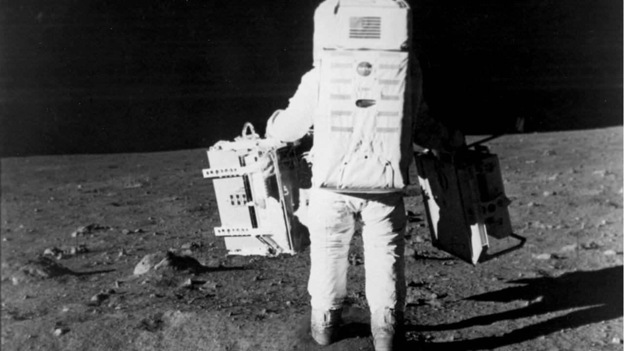 Der Astronaut Edwin E. Aldrin Jr. läuft über die Mondoberfläche und trägt zwei Taschen mit wissenschaftlichem Equipment bei sich.