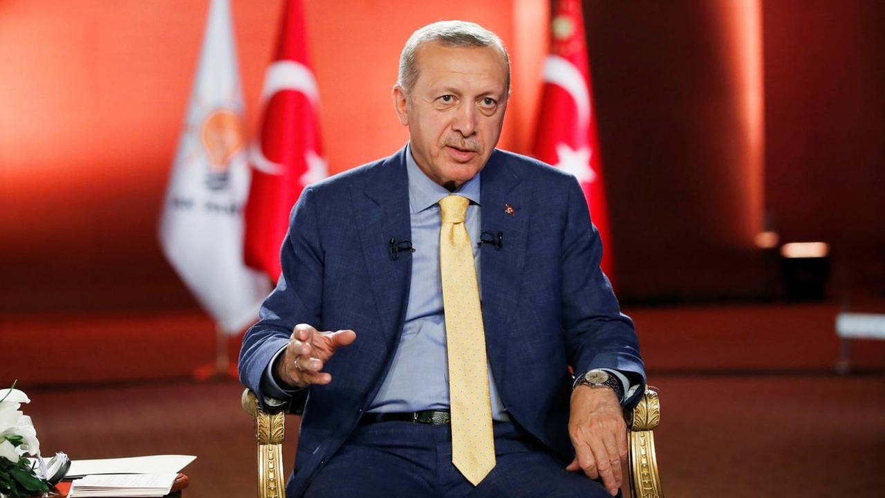 Erdogan sitzt vor türkischer Flagge und spricht