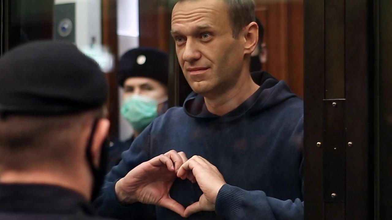 Alexei Nawalny formt mit seinen Händen ein Herz, während er bewacht hinter einer Glasscheibe seht.