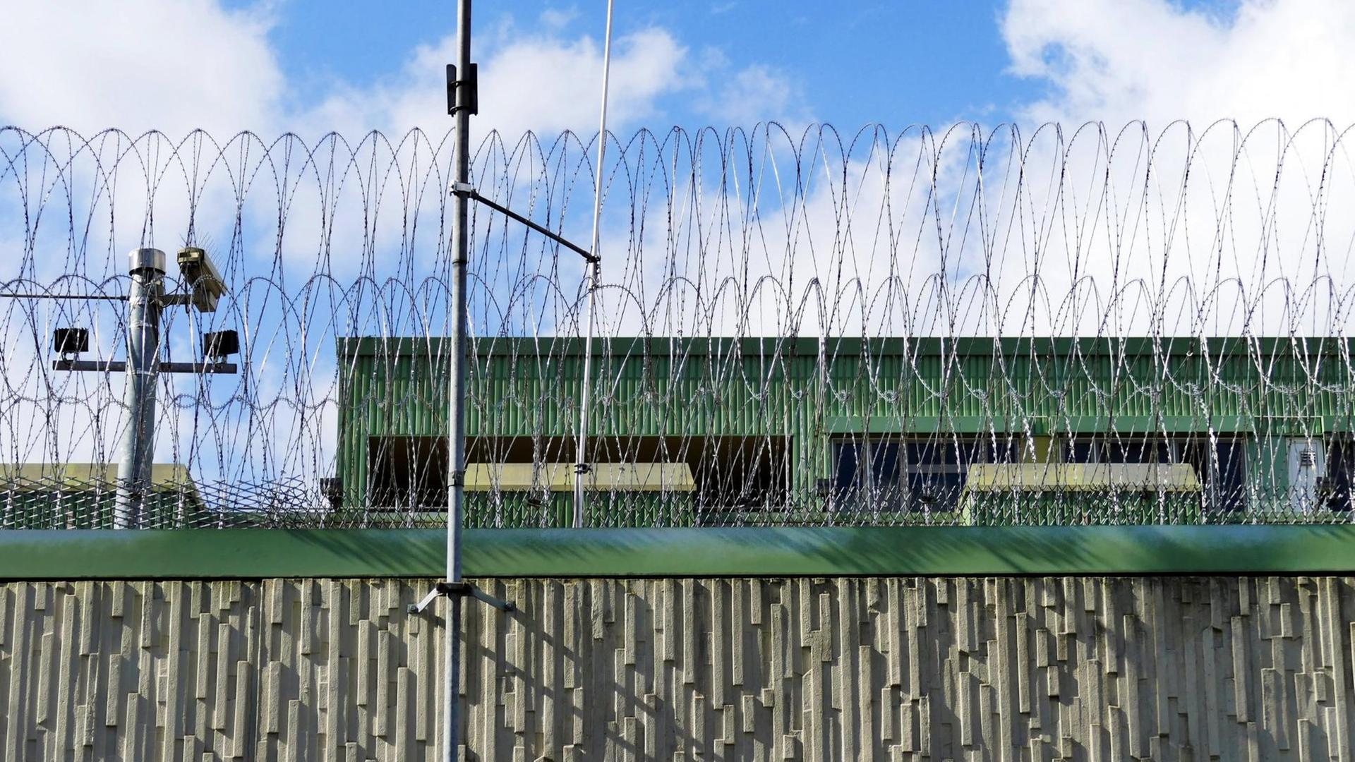 Außenansicht des Justizvollzugskrankenhauses Fröndenberg in Nordrhein-Westfalen. Auf einer hohen Mauer liegt Stacheldraht.