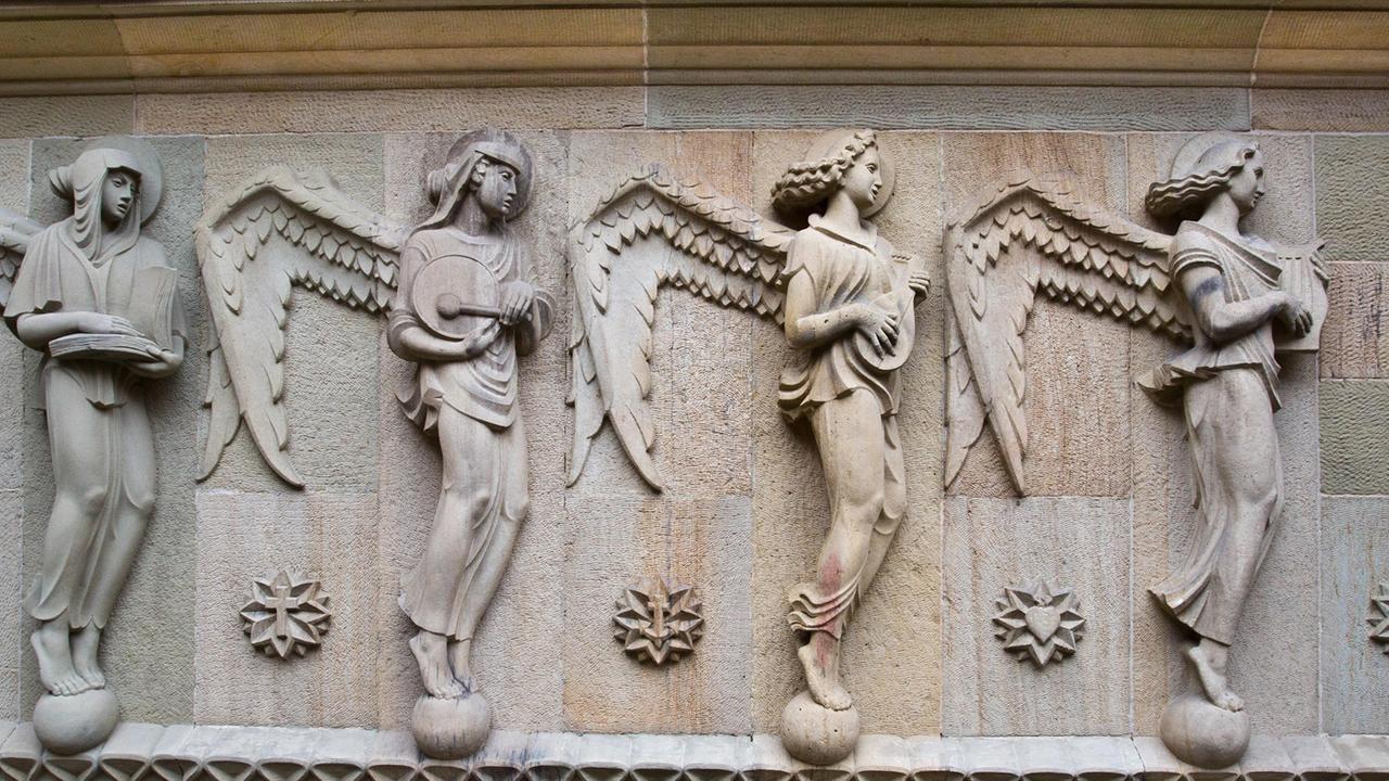 Figurengruppe an der Hauptfassade der Katholischen Kirche St. Fidelis in Stuttgart: Die Attribute dieser vier Engel sind Buch, Tamburin, Laute und Lyra.