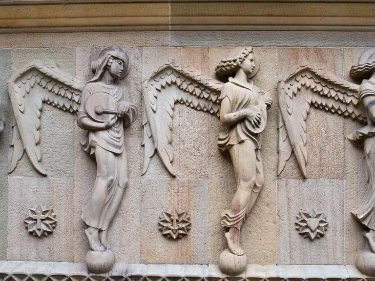 Figurengruppe an der Hauptfassade der Katholischen Kirche St. Fidelis in Stuttgart: Die Attribute dieser vier Engel sind Buch, Tamburin, Laute und Lyra.