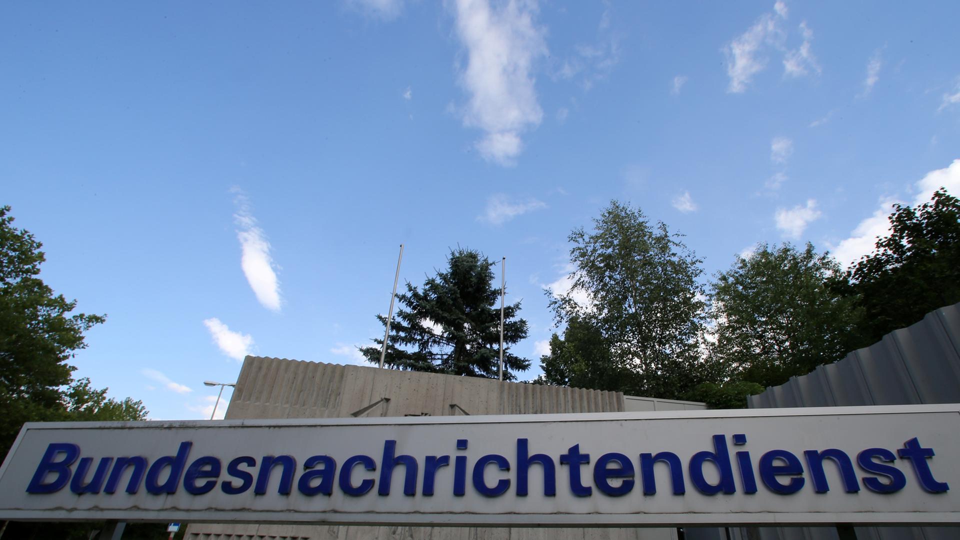 Graues Schild mit blauer Aufschrift "Bundesnachrichtendienst" vor einer grauen Mauer und blauem Himmel