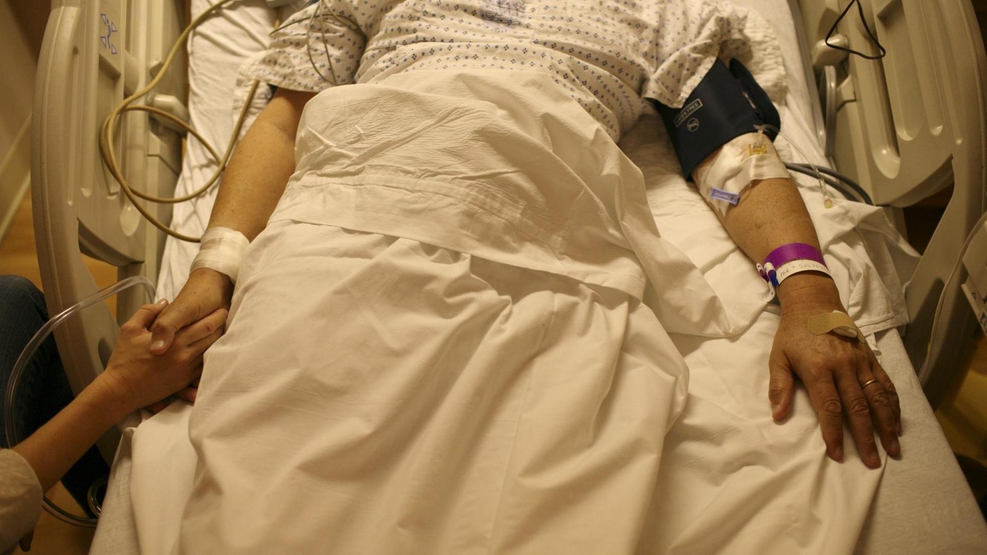Patient in einem Krankenbett, jemand hält seine Hand