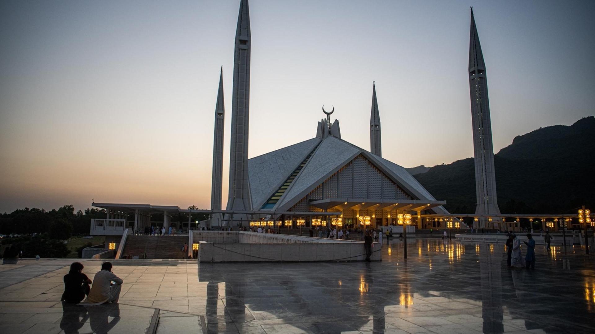 Besucher der Faisal-Moschee in der pakistanischen Hauptstadt Islamabad sitzen bei Sonnenuntergang auf dem Vorplatz der Moschee.