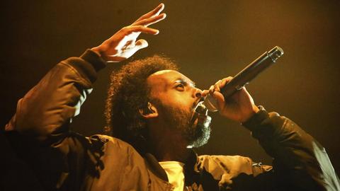 Afrob während eines Live-Auftritts, das Mikrofon in der linken Hand, die rechte Hand gestikulierend.